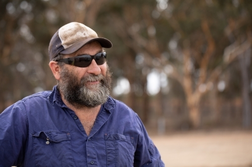 head and shoulders of bearded man wearing sunglasses and cap - Australian Stock Image