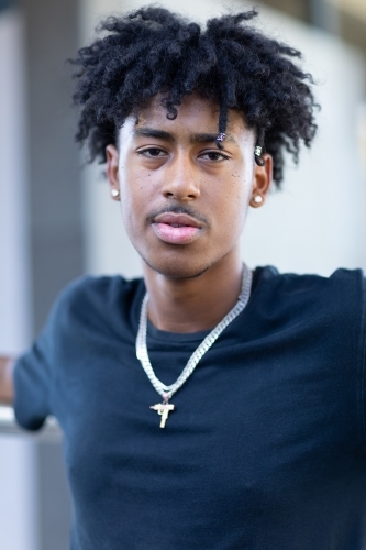 head and shoulders of dark-skinned youth with a mop of black hair wearing a black tee shirt - Australian Stock Image