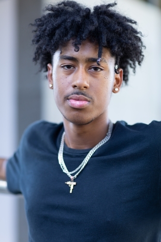 head and shoulders of dark-skinned youth with a mop of black hair wearing a black tee shirt - Australian Stock Image
