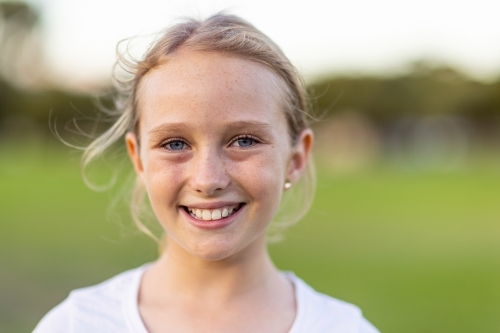 head and shoulders of one blonde-haired blue-eyed child with blurry green background - Australian Stock Image