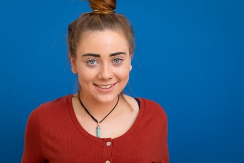 head and shoulders of teenage girl smiling on blue background - Australian Stock Image