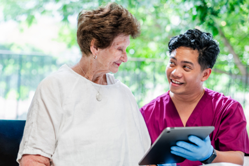 Healthcare worker showing health records using tablet device to an elderly woman - Australian Stock Image