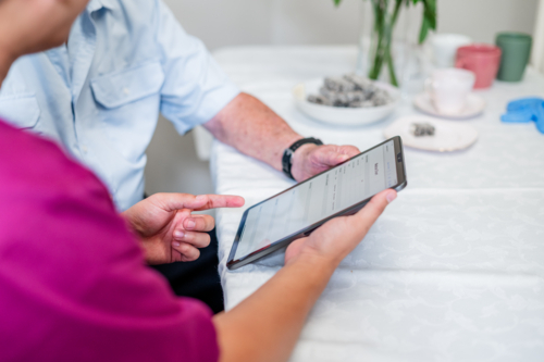 Healthcare worker sits with older male patient sharing information on a tablet device - Australian Stock Image