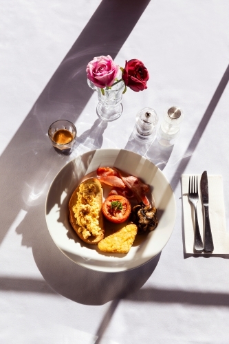 Hearty breakfast meal served in a white plate in a sunlit room. - Australian Stock Image