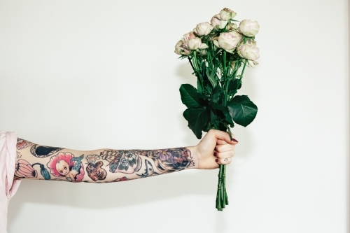 Heavily tattoo'd female arm holding a bunch of thorny pink roses