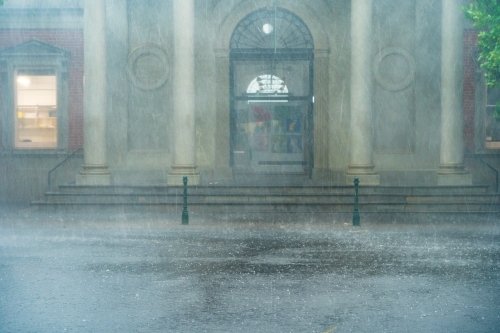 Heavy rain battering the facade of an historic buildings with prominent columns - Australian Stock Image
