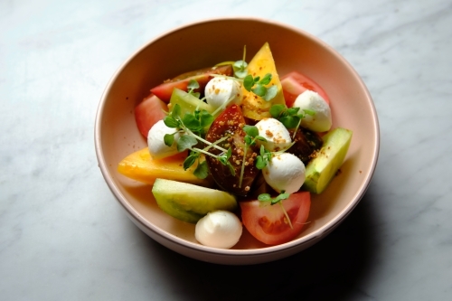 Heirloom tomatoes salad with mozzarella cheese in a pink bowl - Australian Stock Image