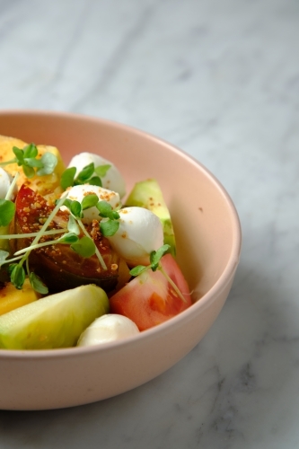 Heirloom tomatoes salad with mozzarella cheese in a pink bowl - Australian Stock Image