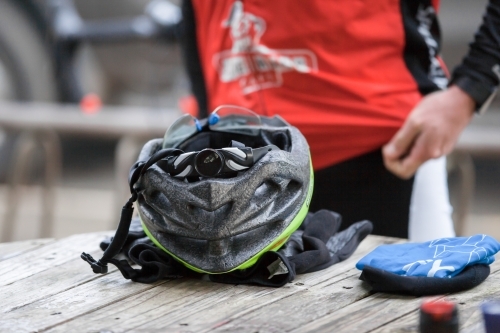 Helmet and gloves on a table at a cafe with a cyclist in background - Australian Stock Image