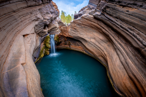 Hidden gorge waterfall plunging into a deep blue rock pool. - Australian Stock Image