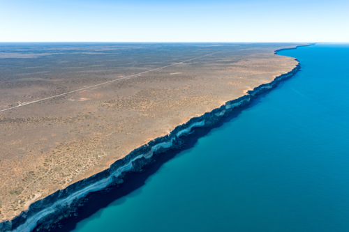 High aerial view of a straight road following the edge of steep limestone cliffs by the ocean - Australian Stock Image