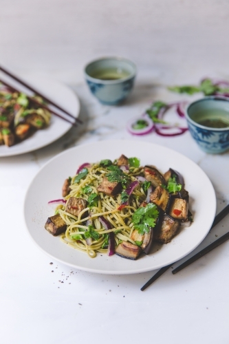 High angle of cold soba noodle, eggplant and parsley salad with green tea on white marble background - Australian Stock Image