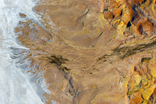 High-angle view of textured salt flats meeting golden sand dunes and dark drainage patterns - Australian Stock Image
