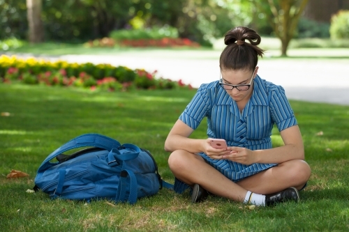 High school student looking at her phone in gardens - Australian Stock Image