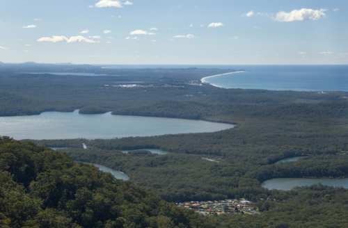 High view of a lake next to beaches and bush with a small village - Australian Stock Image