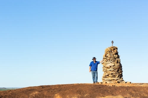 Hiker atop granite outcrop next to rock cairn - Australian Stock Image