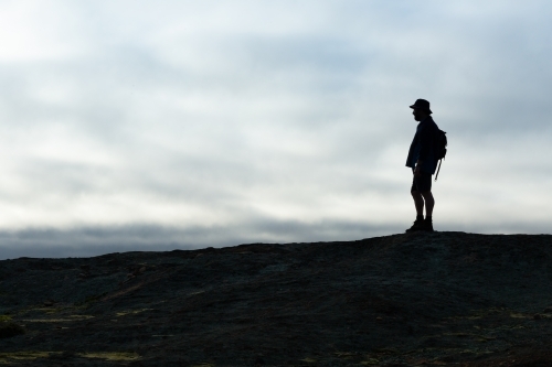 hiker silhouetted against cloudy sky in open landscape - Australian Stock Image