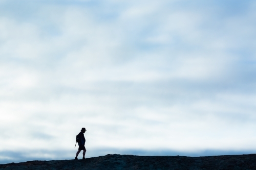 Hiker walking along ridge with soft cloudy sky background