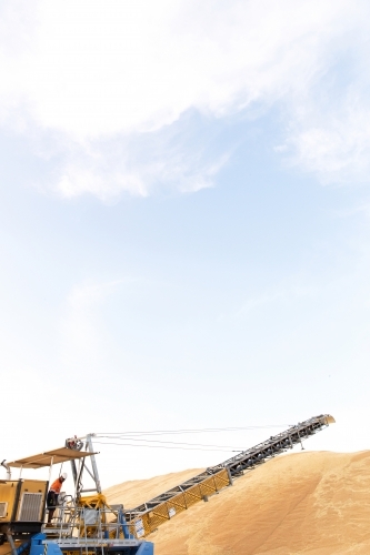Hill of sand and yellow crane with one male operator standing on it - Australian Stock Image