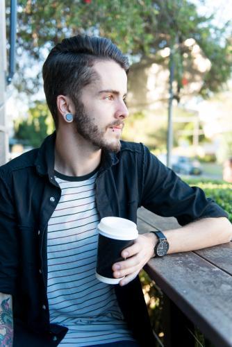 Hipster man sitting outdoors with a take away coffee - Australian Stock Image