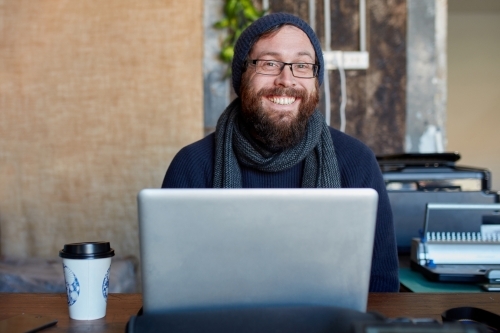 Hipster man with beard smiling at outdoor work table with a laptop