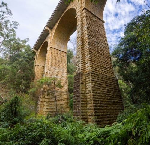 Historic sandstone arch bridge from below, with green bush and clouds - Australian Stock Image