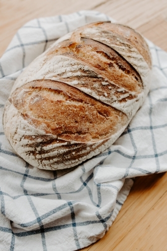 Home made Sour dough bread cooling on a tea towel which is on a wooden chopping board - Australian Stock Image