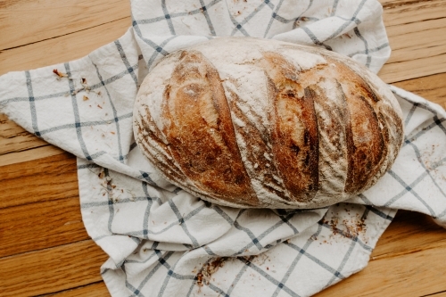 Home made Sour dough bread cooling on a tea towel which is on a wooden chopping platter board - Australian Stock Image