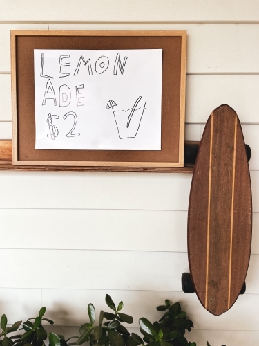 Homemade Lemonade stand sign hanging up with retro skateboard & green plants against weather board - Australian Stock Image