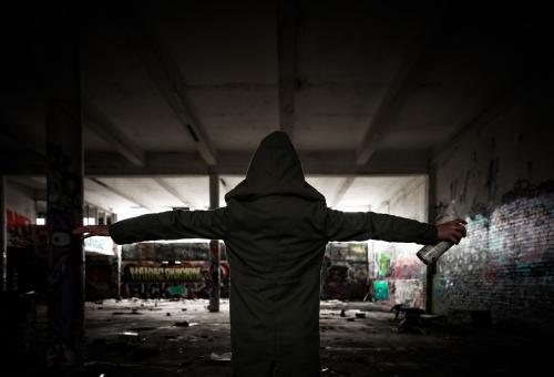 Hooded girl holding spray paint in a pose of defiance