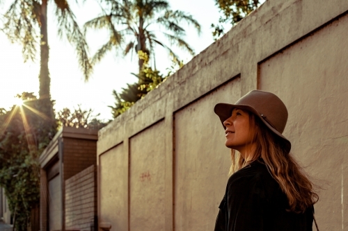 horizonal shot of woman smiling and looking up with a wall, trees and sunlight at the back - Australian Stock Image