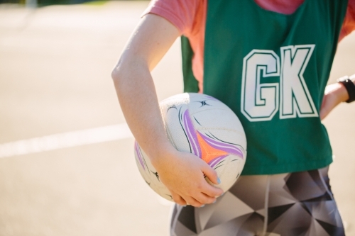 horizontal half body shot of a woman in sports wear holding a net ball in between her hand and waist