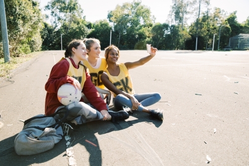 horizontal photo of three young women taking a selfie while sitting on the ground on a sunny day - Australian Stock Image