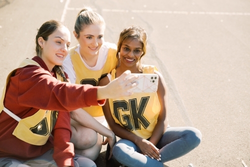 horizontal photo of three young women taking a selfie while sitting on the ground on a sunny day - Australian Stock Image