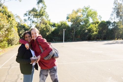 horizontal photo of two young women wearing coat and jacket close to each other on a sunny day - Australian Stock Image