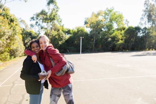 horizontal photo of two young women wearing coat and jacket close to each other on a sunny day - Australian Stock Image