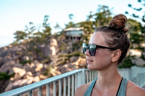 horizontal shot a woman wearing sunglasses looking from a far with trees and balcony at the back - Australian Stock Image