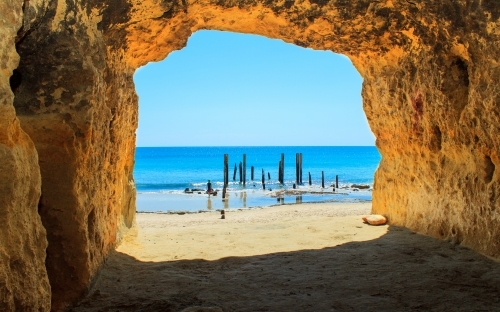 Horizontal shot of a beach cave toward bright blue water on a sunny day - Australian Stock Image