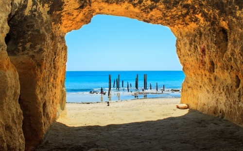 Horizontal shot of a beach cave toward bright blue water on a sunny day