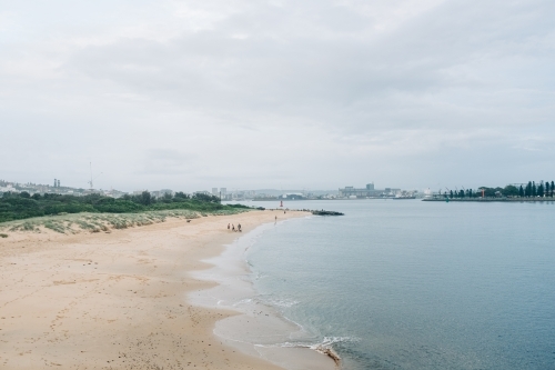 horizontal shot of a beach front with white sand, trees, buildings and people on a gloomy day - Australian Stock Image
