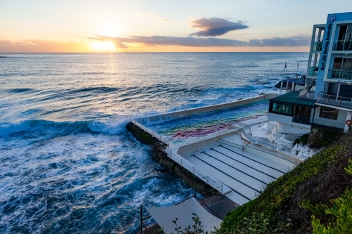horizontal shot of a beach house with waves with cloudy skies and sunset in the background - Australian Stock Image