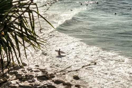 horizontal shot of a beach with waves and a person holding a surfboard - Australian Stock Image