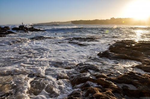 horizontal shot of a beach with waves, rocks and sunlight with clear skies - Australian Stock Image