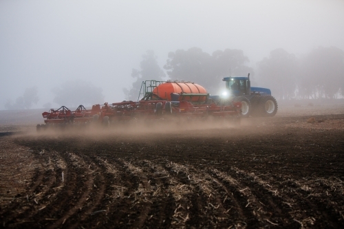 Horizontal shot of a blue tractor cultivating the soil in the field. - Australian Stock Image