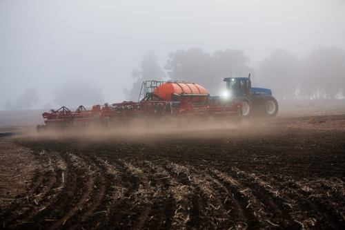 Horizontal shot of a blue tractor cultivating the soil in the field.