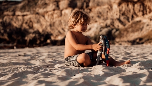 Horizontal shot of a boy playing with his toys in the sand