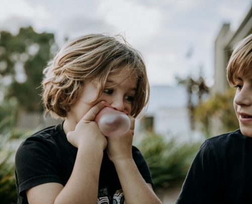 Horizontal shot of a boy watching a kid blow bubblegum - Australian Stock Image