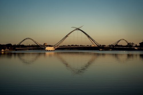 horizontal shot of a bridge with wavy structures reflecting in a body of water with clear skies - Australian Stock Image