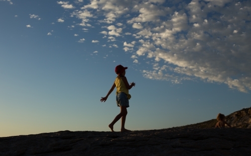 Horizontal shot of a child walking along hilltop at dusk - Australian Stock Image