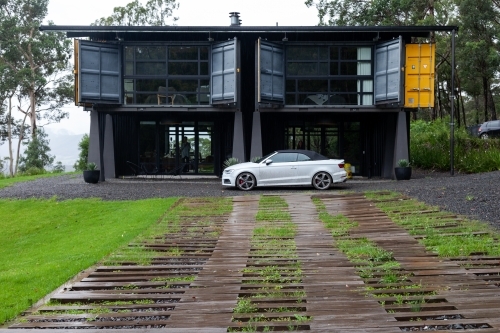 horizontal shot of a house with open windows, white car and wet ground with green grass